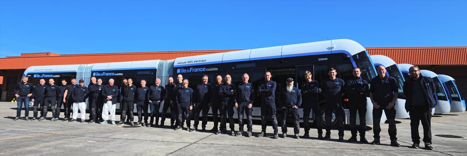 The team behind a 24-metre electric bus stands side by side along its full length — the people it takes to build the bus forming a 24-metre line themselves.